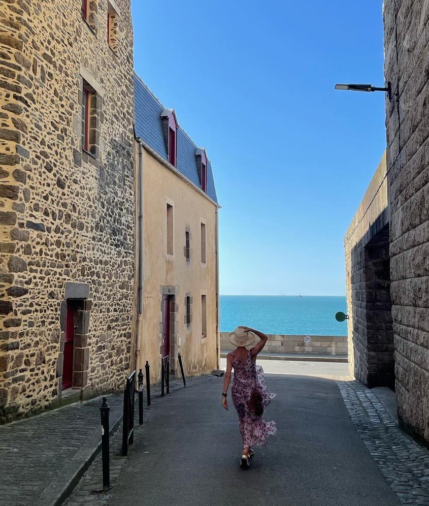 Ruelle typique en pierres de taille s'ouvrant sur la mer sous un ciel bleu azur.